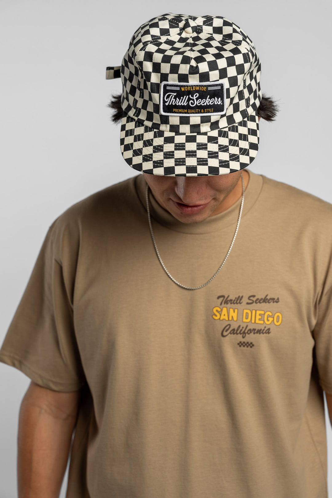 Person wearing a black checkered cap with a 'Thrill Seekers' logo