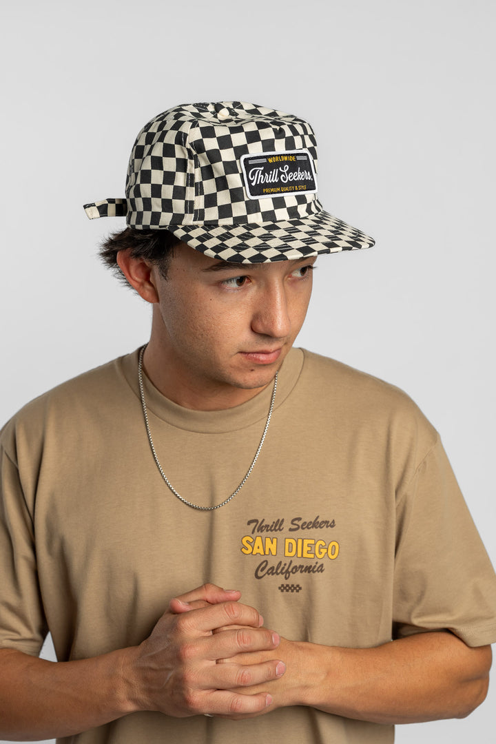Person wearing a black checkered cap with a 'Thrill Seekers' logo