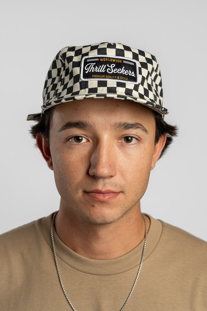 Person wearing a black checkered cap with a 'Thrill Seekers' logo