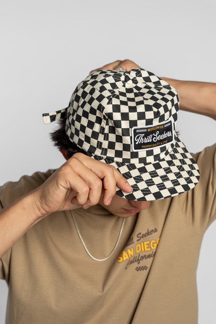Person wearing a black checkered cap with a 'Thrill Seekers' logo