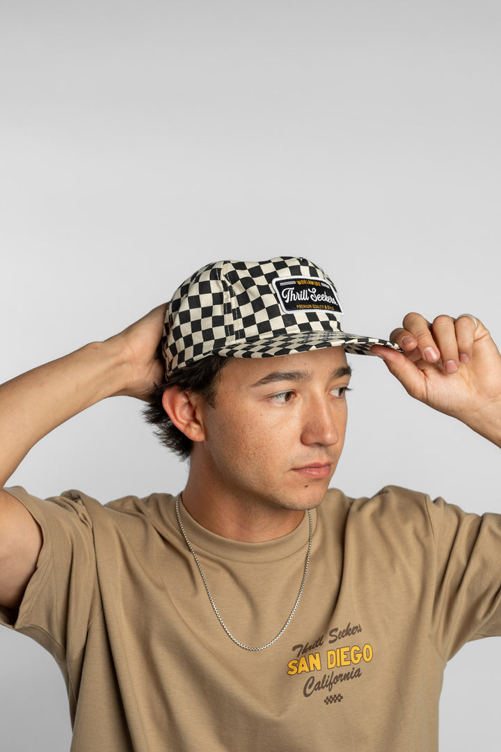Person wearing a black checkered cap with a 'Thrill Seekers' logo