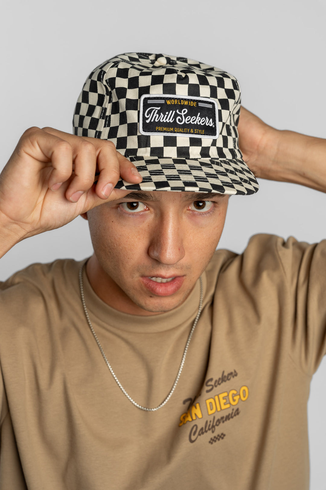 Person wearing a black checkered cap with a 'Thrill Seekers' logo