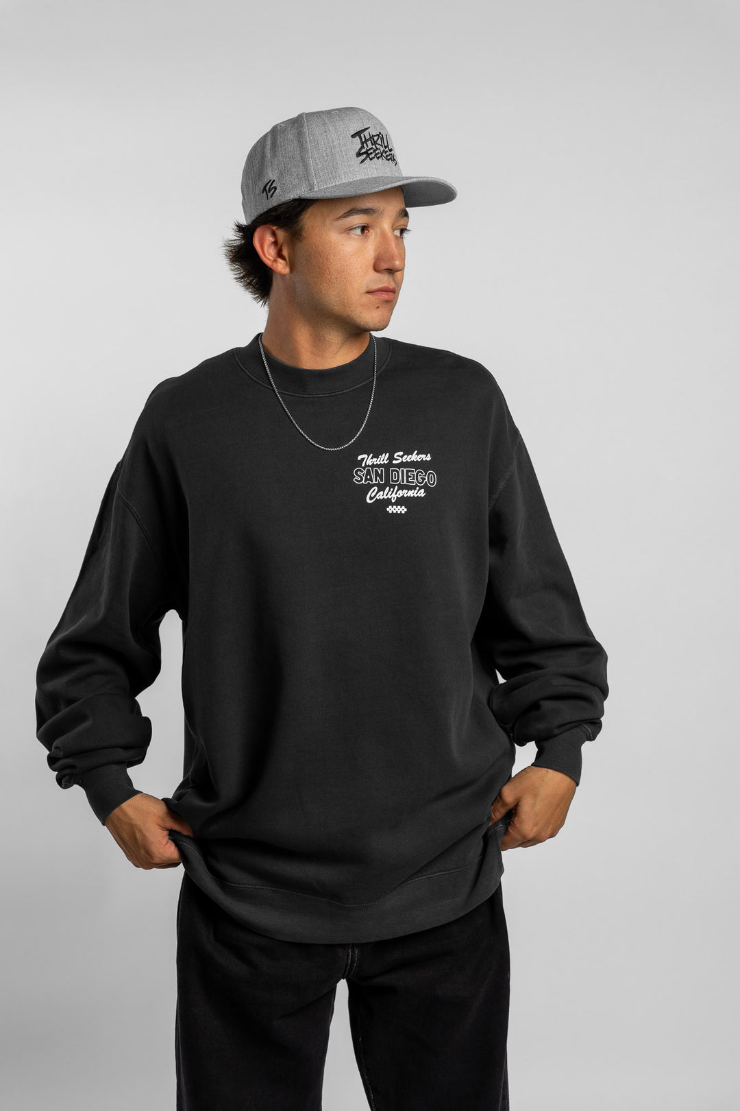 Person wearing faded black crewneck with 'Thrill Seekers' shop logo