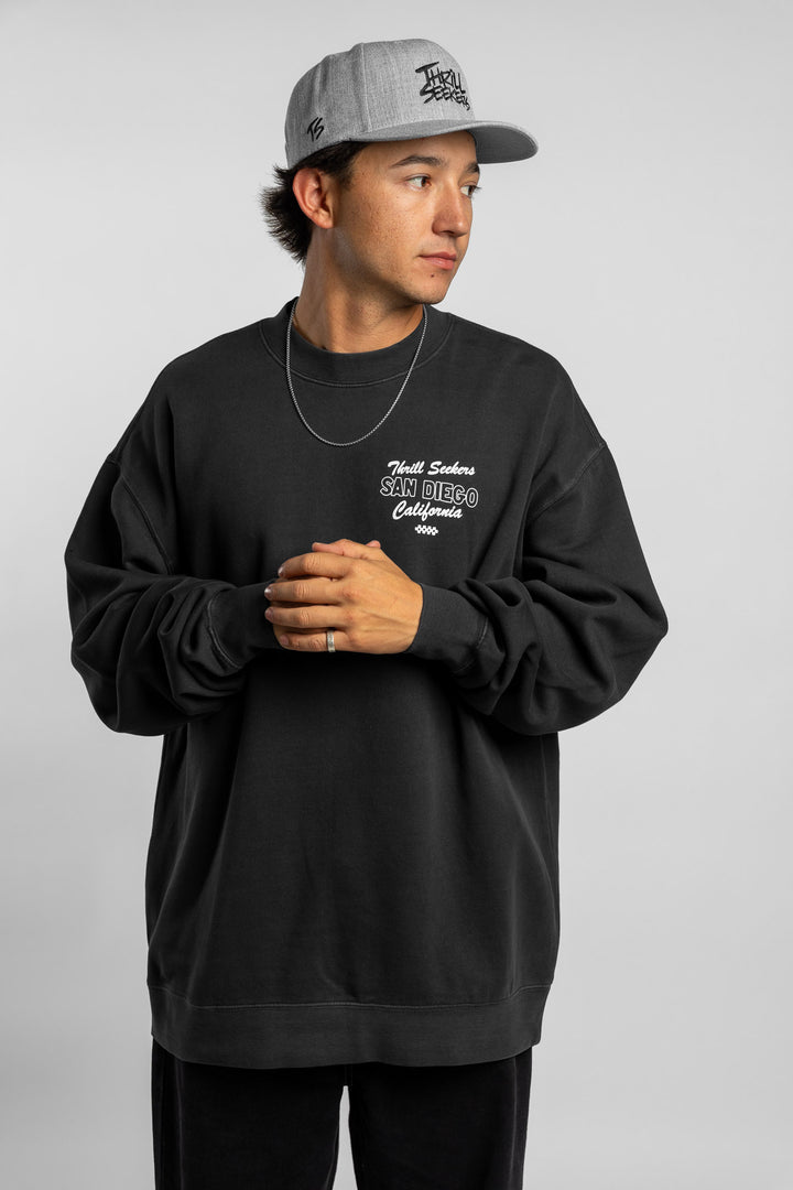 Person wearing faded black crewneck with 'Thrill Seekers' shop logo