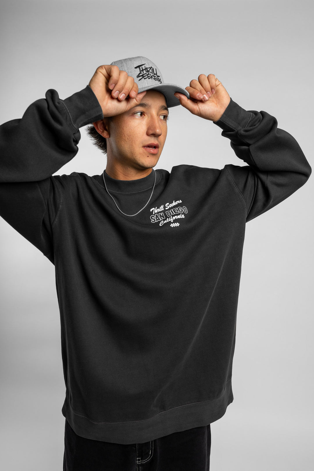 Person wearing faded black crewneck with 'Thrill Seekers' shop logo