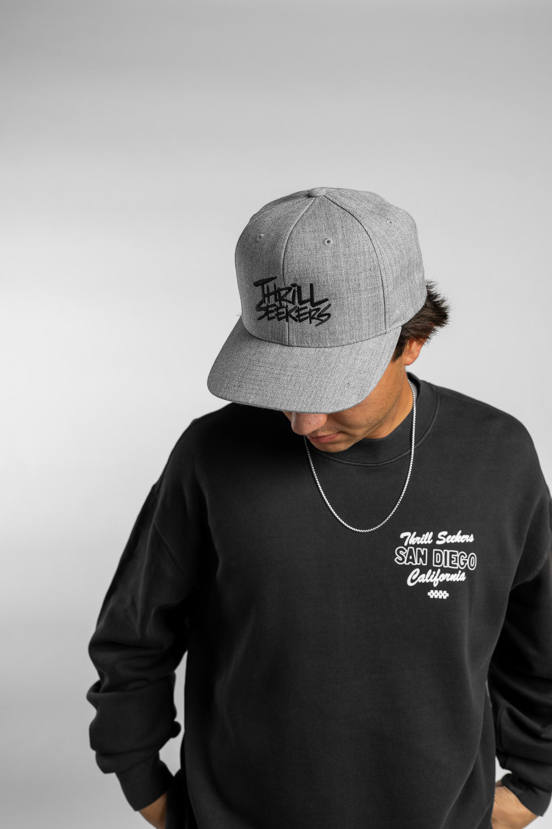 Person wearing faded black crewneck with 'Thrill Seekers' shop logo