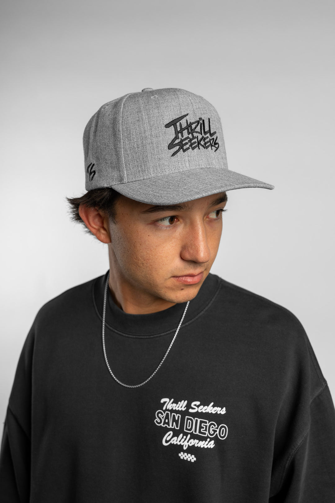Person wearing a grey snapback hat with 'Thrill Seekers' logo in black