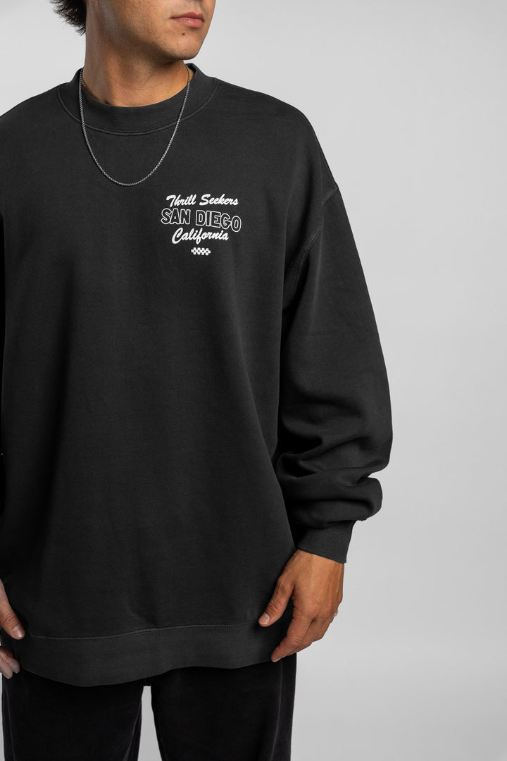 Person wearing faded black crewneck with 'Thrill Seekers' shop logo