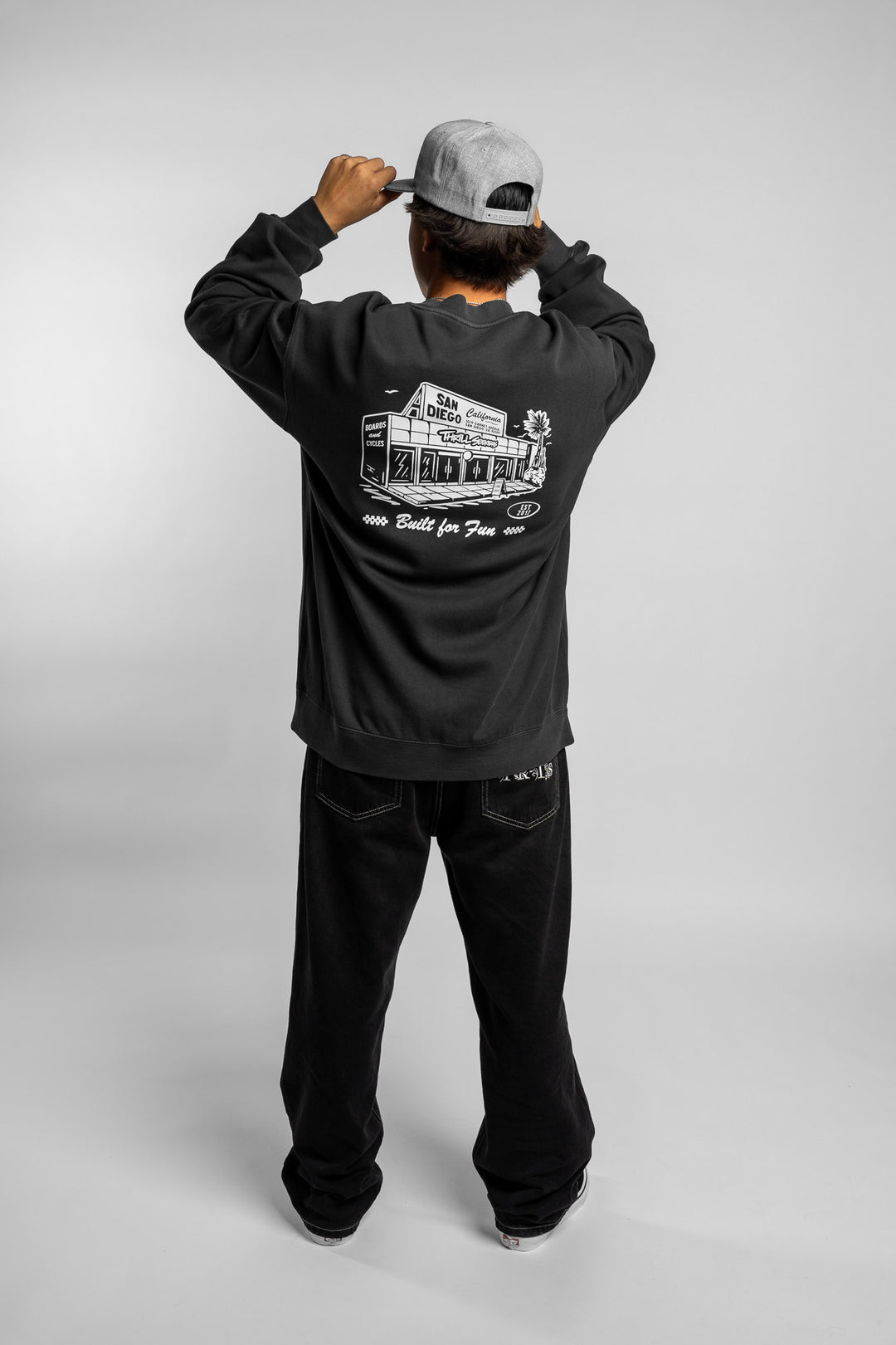 Person wearing faded black crewneck with 'Thrill Seekers' shop logo