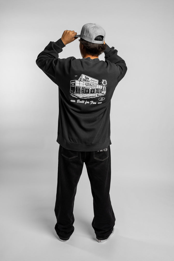 Person wearing faded black crewneck with 'Thrill Seekers' shop logo