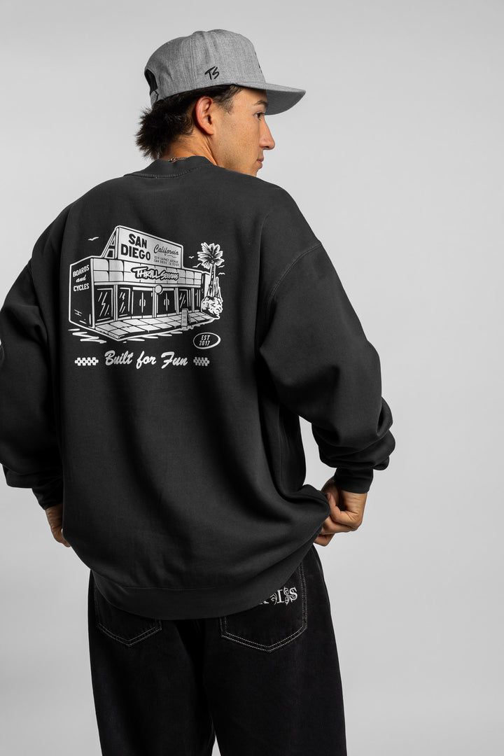 Person wearing faded black crewneck with 'Thrill Seekers' shop logo