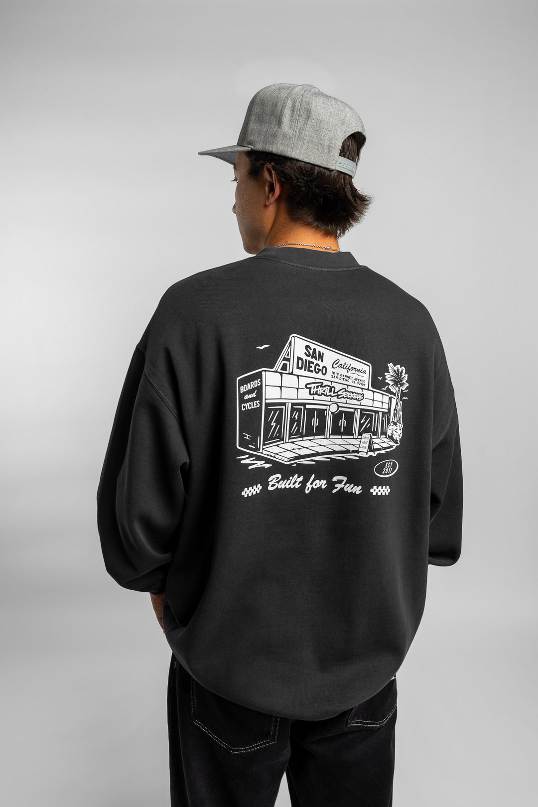 Person wearing faded black crewneck with 'Thrill Seekers' shop logo