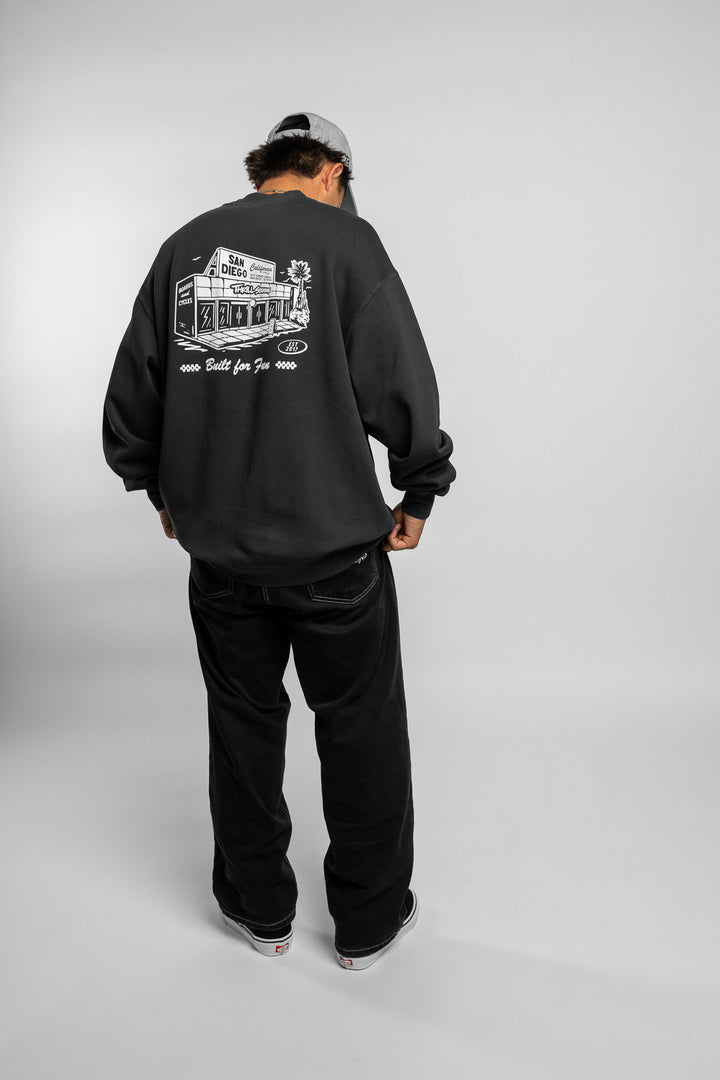 Person wearing faded black crewneck with 'Thrill Seekers' shop logo