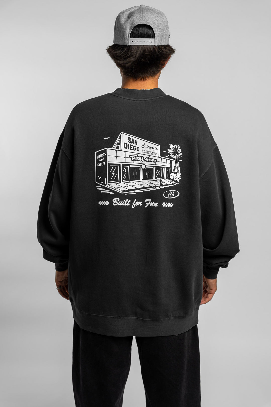 Person wearing faded black crewneck with 'Thrill Seekers' shop logo