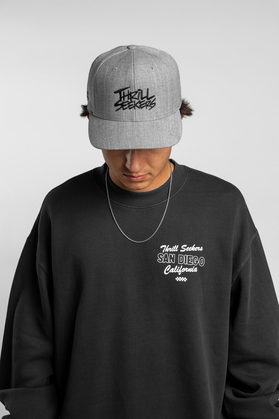 Person wearing a grey snapback hat with 'Thrill Seekers' logo in black
