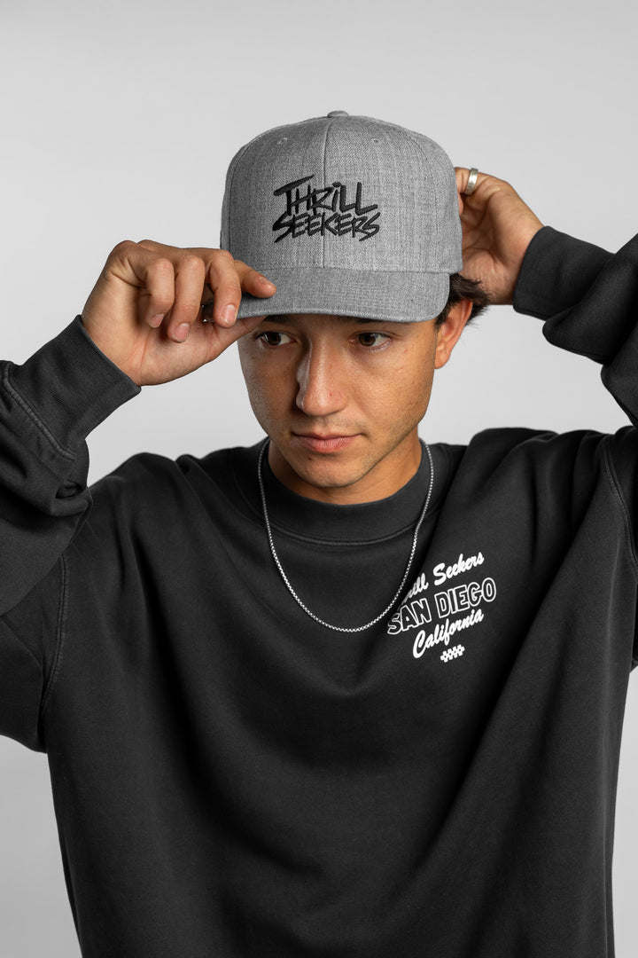 Person wearing a grey snapback hat with 'Thrill Seekers' logo in black