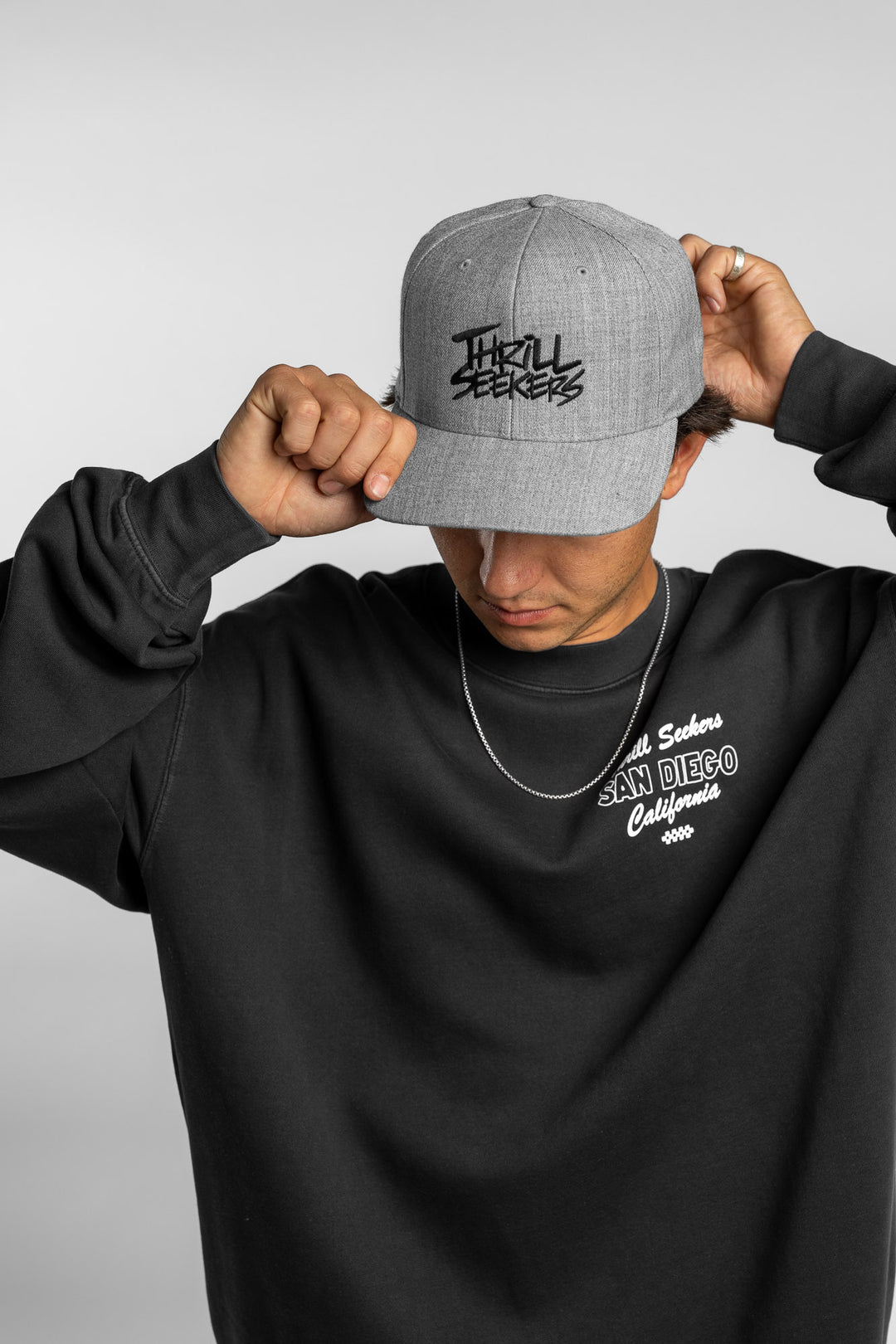 Person wearing a grey snapback hat with 'Thrill Seekers' logo in black