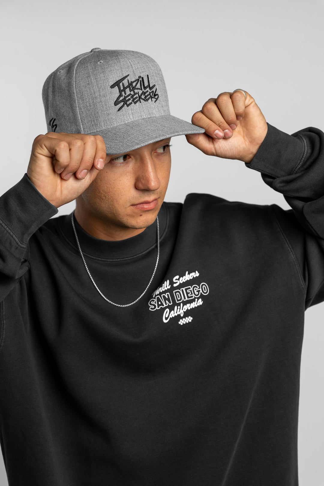 Person wearing a grey snapback hat with 'Thrill Seekers' logo in black
