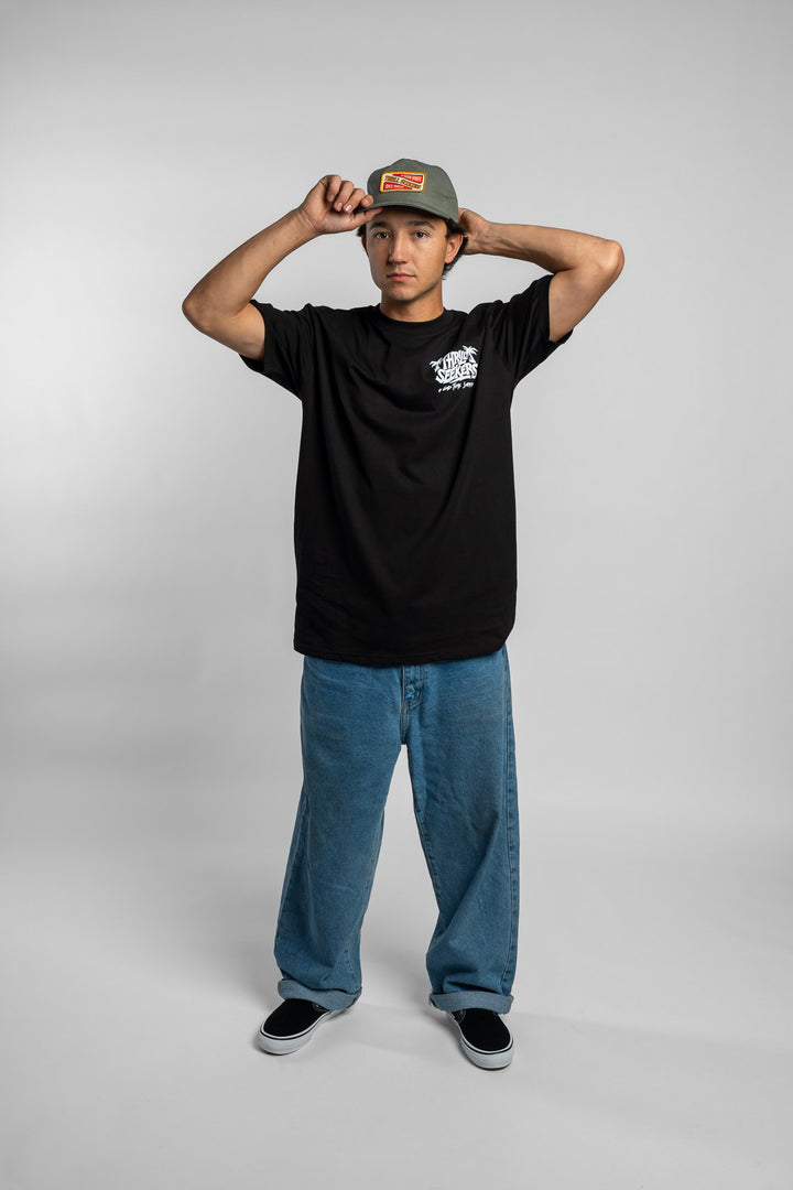 Person wearing a black t-shirt with a green 'Thrill Seekers' logo cap on a white background