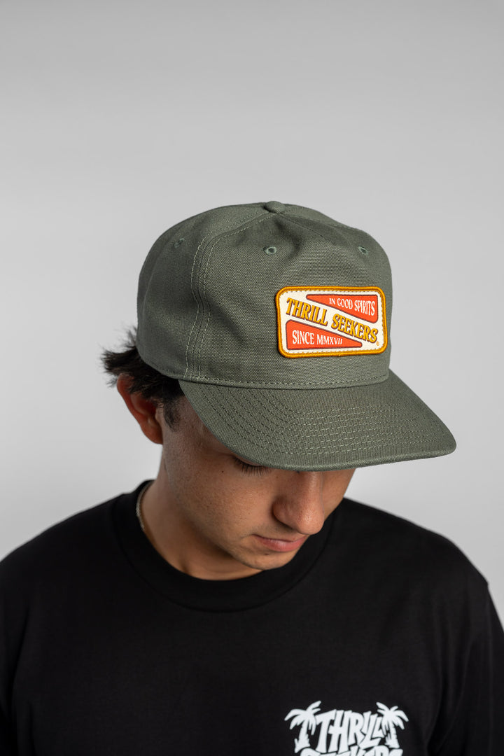 Person wearing a black t-shirt with a green 'Thrill Seekers' logo cap on a white background