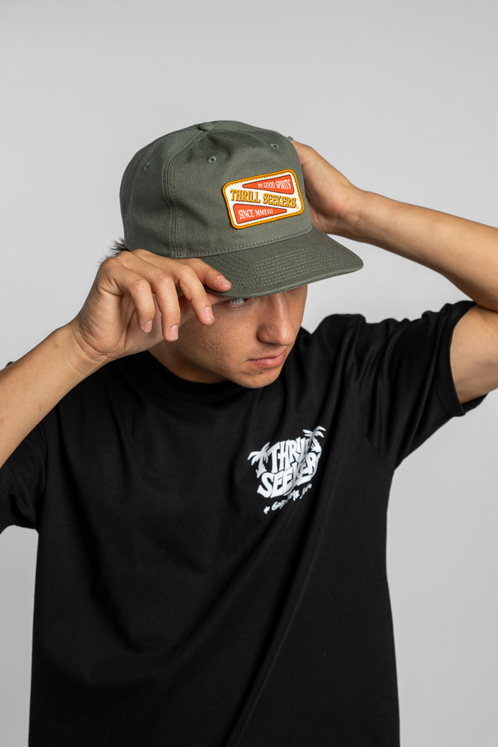 Person wearing a black t-shirt with a green 'Thrill Seekers' logo cap on a white background