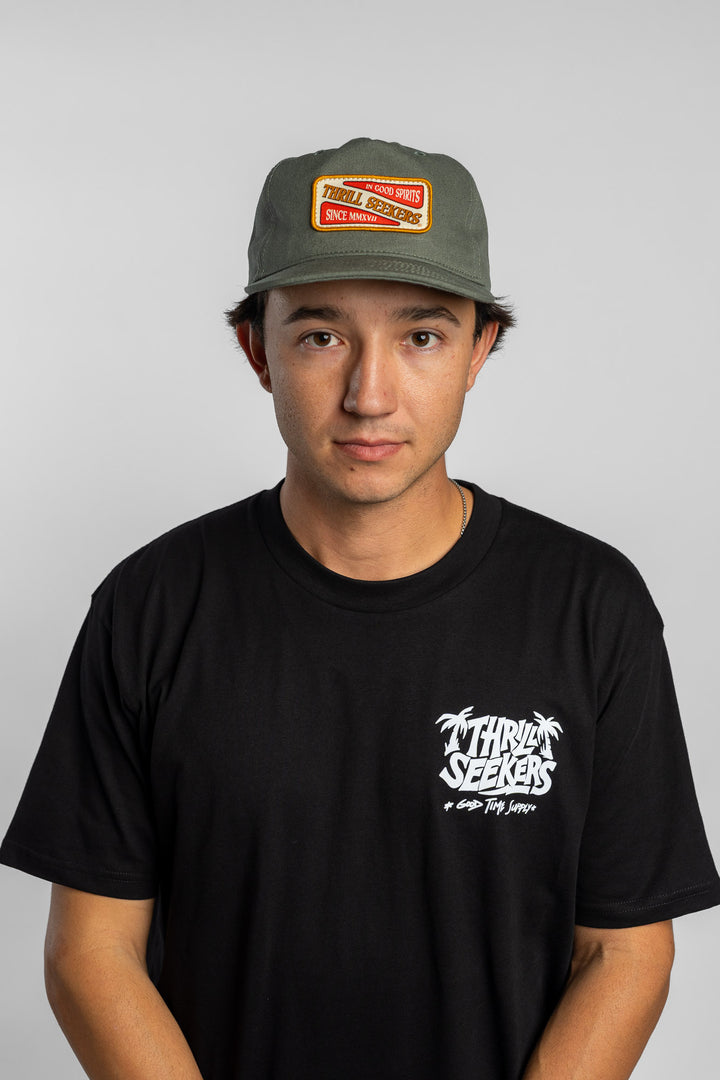 Person wearing a black t-shirt with a green 'Thrill Seekers' logo cap on a white background